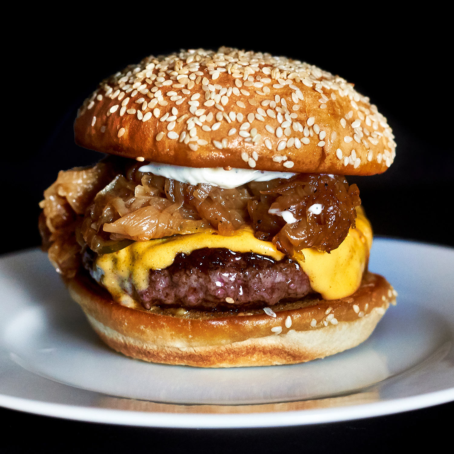 A Richard Eaglespoon burger on a black background and also on a plate. Featuring more caramelized onions than sense.