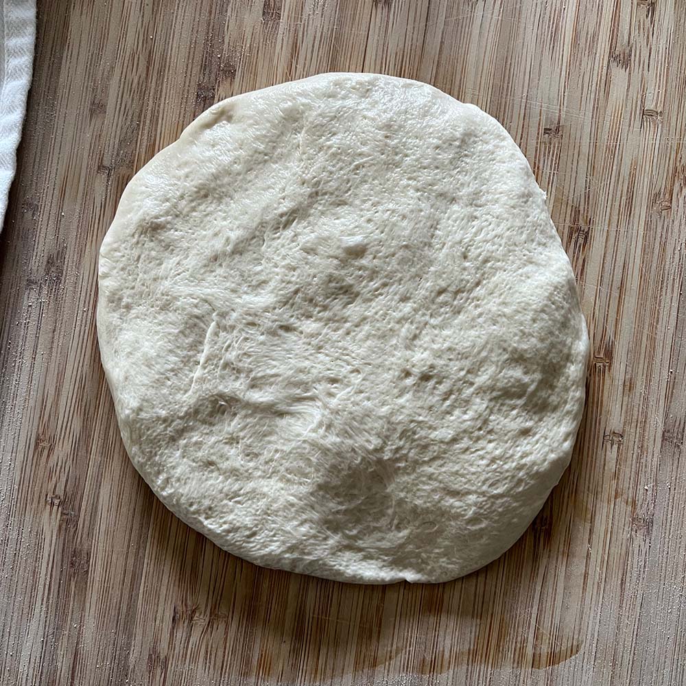 Dough removed from proofing container and flattened, sticky-side up.